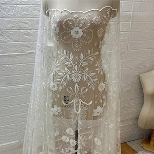 May include: White beaded lace fabric with floral designs and a scalloped edge. The fabric is displayed on a white mannequin.