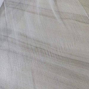 May include: White sheer fabric with a textured, striped pattern. The fabric is draped over a light brown surface.