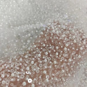 May include: White beaded fabric with a delicate mesh backing. The beads are small and round, creating a shimmering effect.