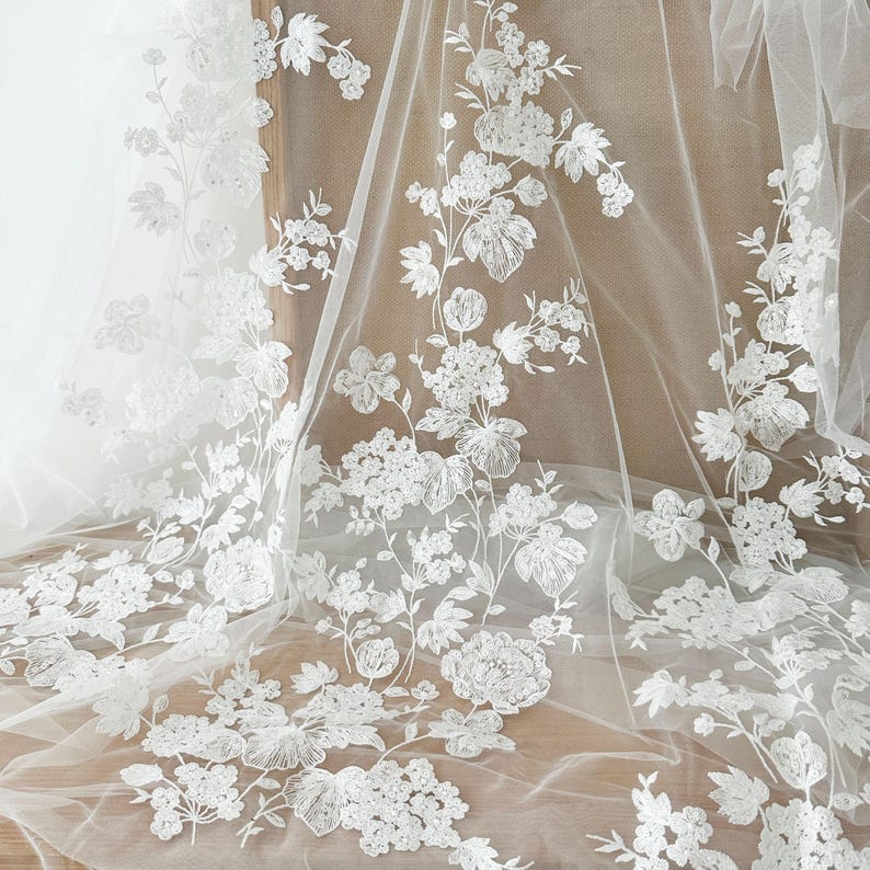 May include: White floral lace fabric with a delicate pattern of flowers and leaves. The lace is on a sheer mesh background.