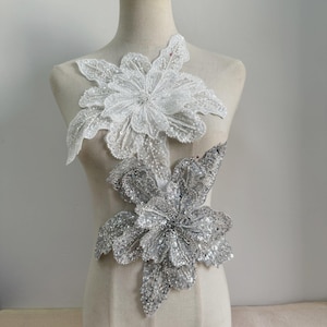 May include: Two large floral appliques, one white and one silver, with sequins and beads. The appliques are ideal for adding a touch of elegance to clothing or crafts.