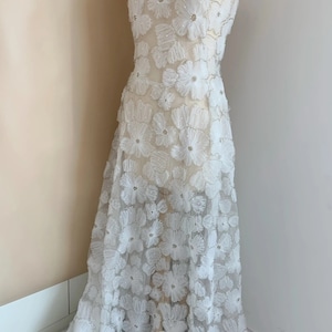 May include: White floral lace fabric with 3D flowers and a sheer background. The fabric is delicate and intricate, perfect for wedding dresses, evening gowns, or other special occasion garments.