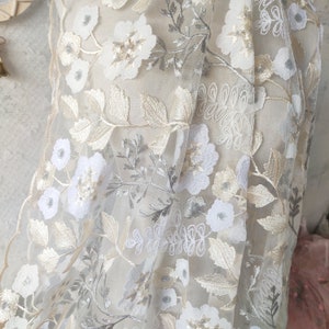 May include: White and silver floral embroidery on a sheer beige fabric. The embroidery features delicate flowers and leaves.