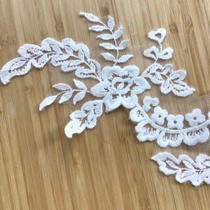 May include: White lace applique with floral and leaf designs. The lace is delicate and intricate, with a sheer background.