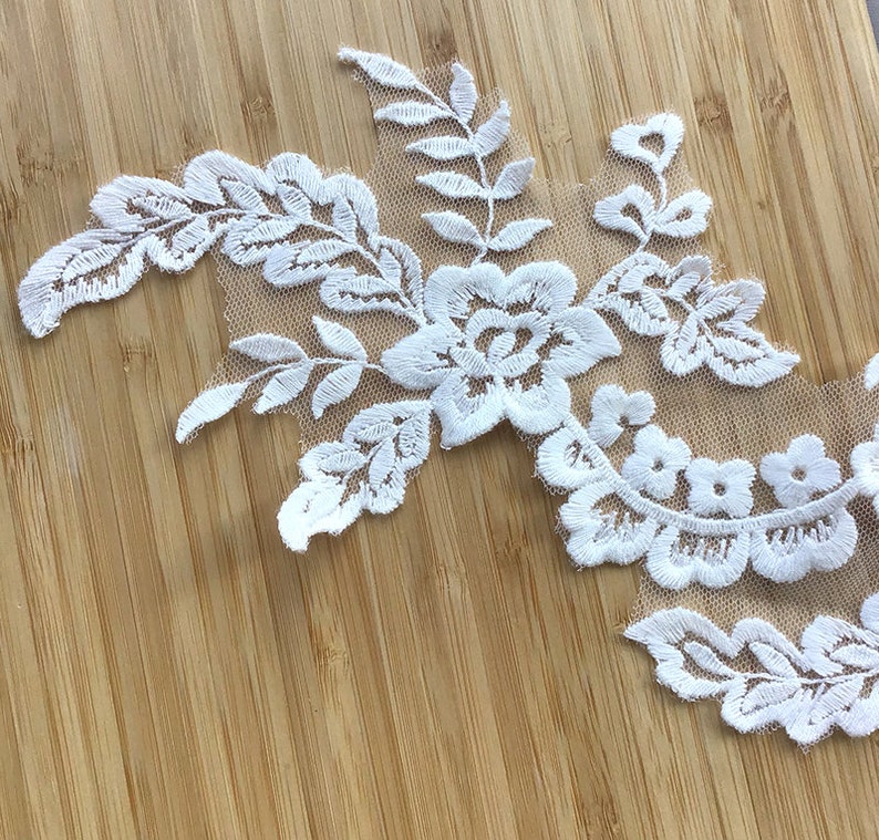 May include: White lace applique with floral and leaf designs. The lace is delicate and intricate, with a sheer background.