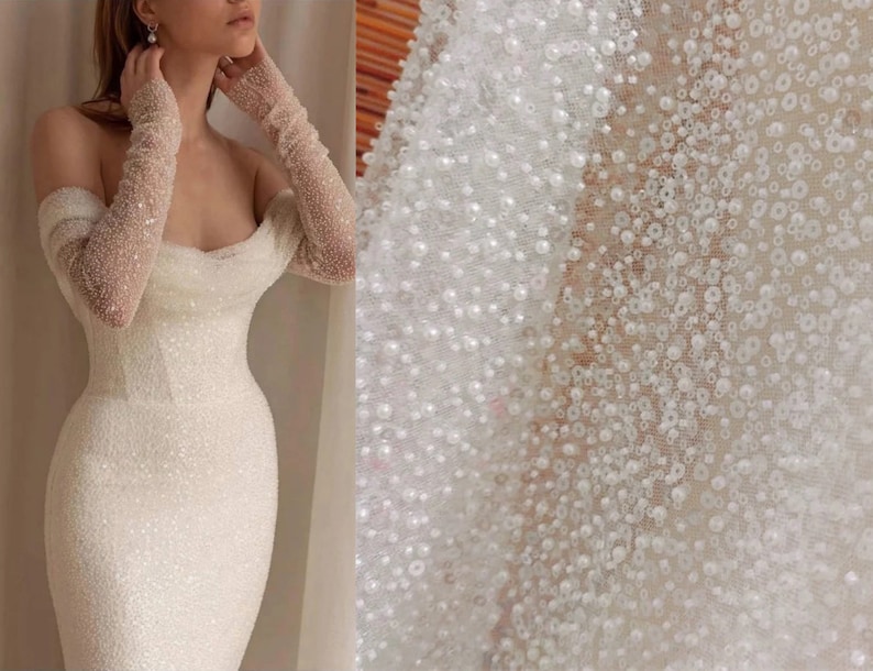 May include: White off-the-shoulder dress with long sleeves made of a beaded fabric. The fabric is a sheer mesh with small white beads sewn onto it.