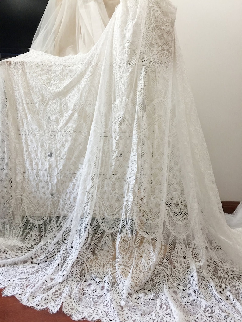 May include: White lace fabric with a delicate floral pattern. The lace is sheer and has a soft, flowing texture.