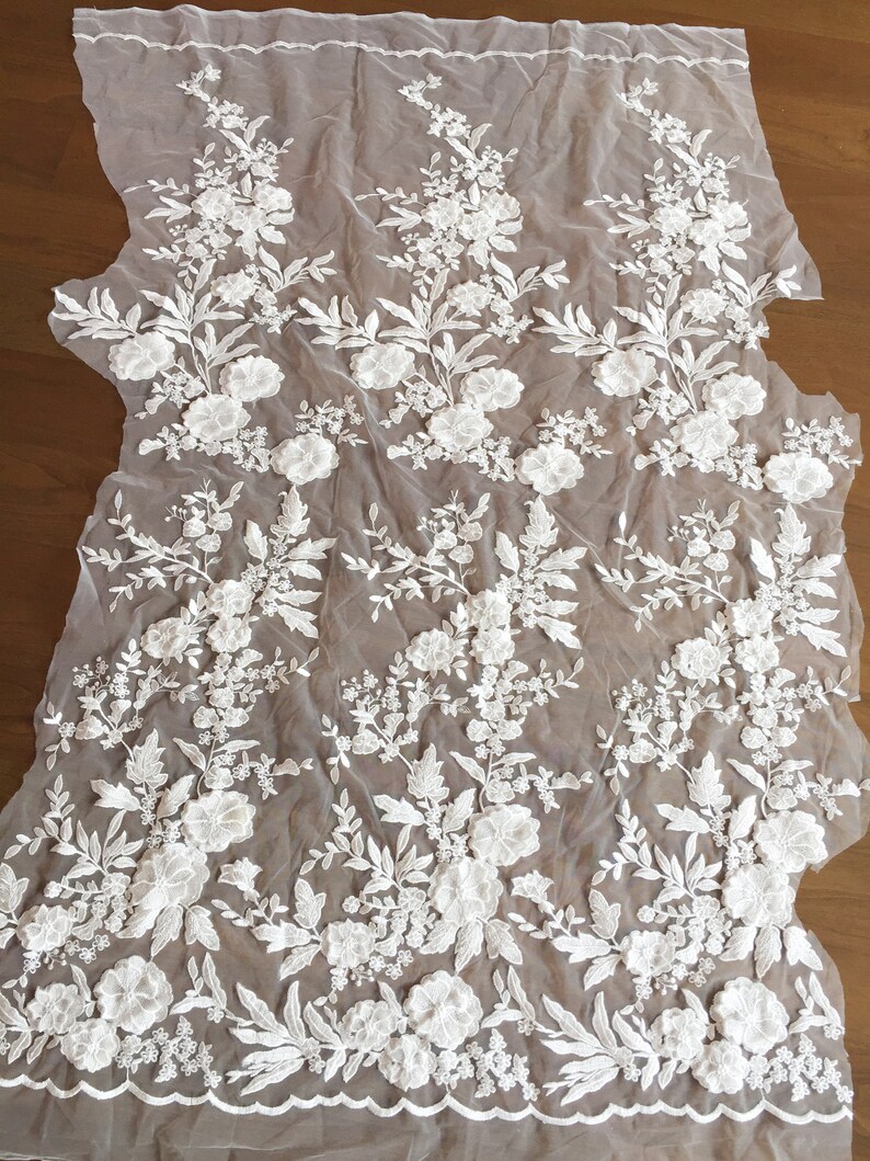 May include: White floral lace fabric with a textured, raised design. The lace is on a sheer, white mesh background.