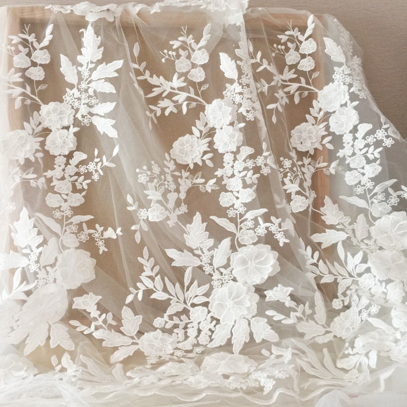 May include: White floral lace fabric with a delicate pattern of flowers and leaves. The lace is on a sheer, ivory background.