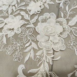 May include: White floral lace fabric with 3D flowers and sequins. The lace is on a sheer mesh background.
