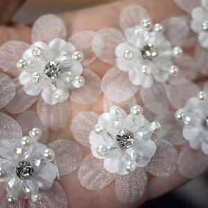 May include: White fabric flower embellishments with pearl and crystal accents.
