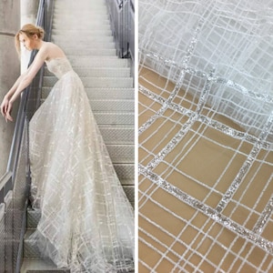 May include: White tulle fabric with a silver sequin grid pattern. The fabric is sheer and delicate, with a soft, flowing texture.