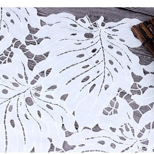 May include: White lace fabric with a delicate floral pattern. The fabric has a cut-out design, creating a delicate and airy look.