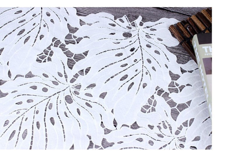 May include: White lace fabric with a delicate floral pattern. The fabric has a cut-out design, creating a delicate and airy look.
