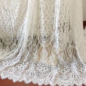 May include: White lace fabric with a delicate floral pattern. The lace has a scalloped edge and is perfect for crafting, sewing, or decorating.