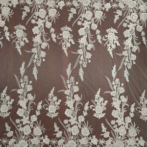 May include: White floral lace fabric with a beaded design. The lace has a delicate floral pattern with small, white beads scattered throughout. The fabric is sheer and has a soft, flowing texture.