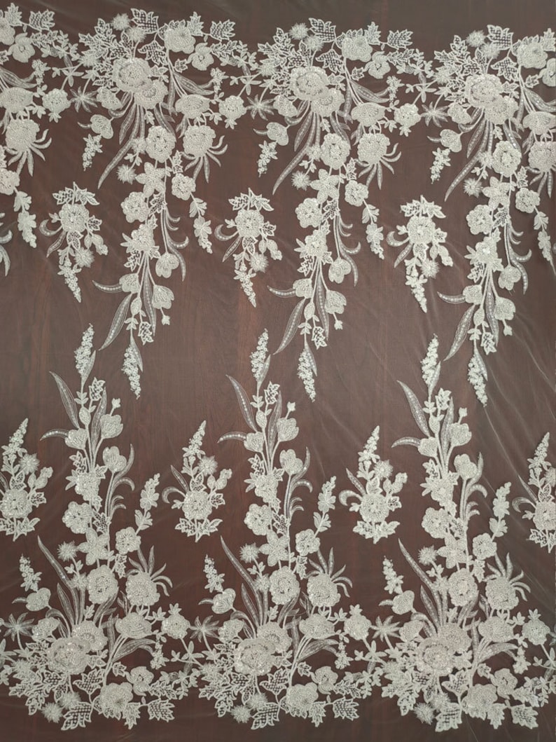 May include: White floral lace fabric with a beaded design. The lace has a delicate floral pattern with small, white beads scattered throughout. The fabric is sheer and has a soft, flowing texture.