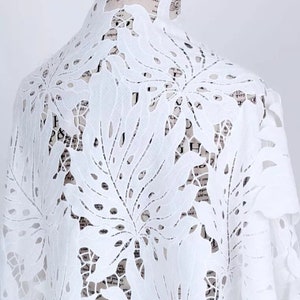 May include: White cotton fabric with a delicate, intricate laser-cut design of large leaves. The fabric is sheer and lightweight, perfect for creating garments or home decor.
