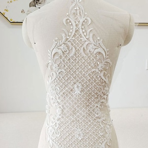 May include: White lace applique featuring a floral design and a grid pattern. The lace is delicate and intricate, and would be ideal for adding a touch of elegance to a wedding dress or other special occasion garment.