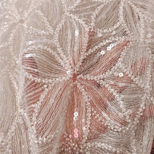 Peut inclure: Tissu de dentelle blanc perl&eacute; et paillet&eacute; avec un motif floral. Le tissu est d&eacute;licat et complexe, avec de petites perles et paillettes blanches &eacute;parpill&eacute;es.