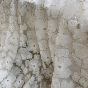 May include: White fabric with a delicate floral pattern. The fabric is embellished with small pearls and has a 3D effect.