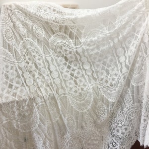 May include: White lace fabric with a delicate, intricate pattern. The lace has a scalloped edge and is perfect for crafting, sewing, or home decor.