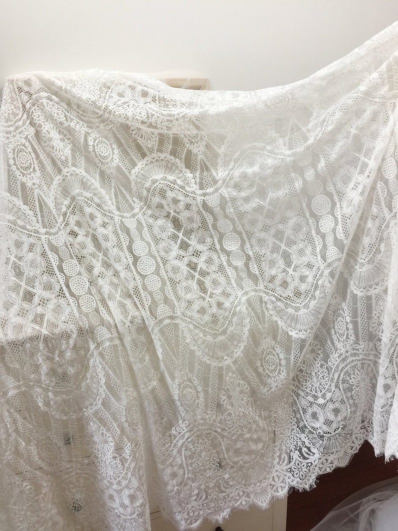 May include: White lace fabric with a delicate, intricate pattern. The lace has a scalloped edge and is perfect for crafting, sewing, or home decor.