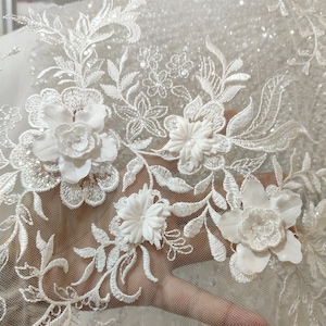 May include: White floral lace fabric with 3D flowers and a glittery background.