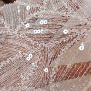Peut inclure: Tissu blanc transparent avec de petites paillettes et perles blanches. Le tissu a une texture d&eacute;licate et dentel&eacute;e.