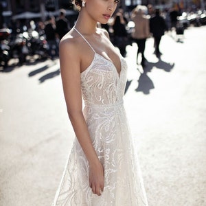 May include: A white lace wedding dress with a plunging neckline and a fitted bodice. The dress has a flowing skirt with delicate floral embroidery.