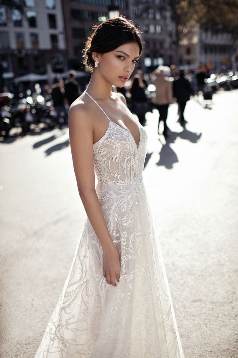 May include: A white lace wedding dress with a plunging neckline and a fitted bodice. The dress has a flowing skirt with delicate floral embroidery.