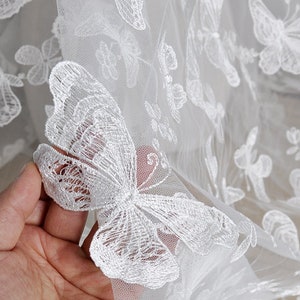 Pu&ograve; includere: Tessuto di pizzo bianco con motivi di farfalle ricamate. Il tessuto &egrave; trasparente e delicato, con una texture morbida e fluida.
