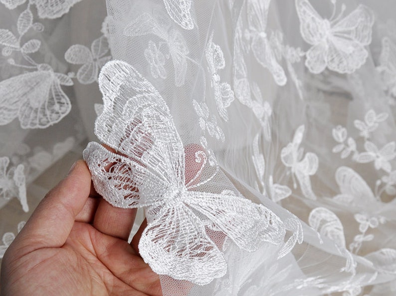 Pu&ograve; includere: Tessuto di pizzo bianco con motivi di farfalle ricamate. Il tessuto &egrave; trasparente e delicato, con una texture morbida e fluida.