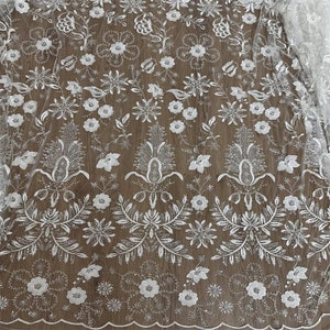 May include: White floral lace fabric with a glittery finish. The lace features a repeating pattern of flowers, leaves, and vines. The fabric is sheer and delicate, and would be perfect for a wedding dress or other special occasion garment.