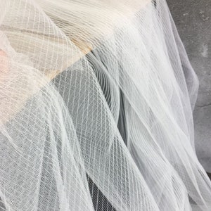 May include: White tulle fabric with a striped pattern. The fabric is soft and sheer, and it has a delicate texture.