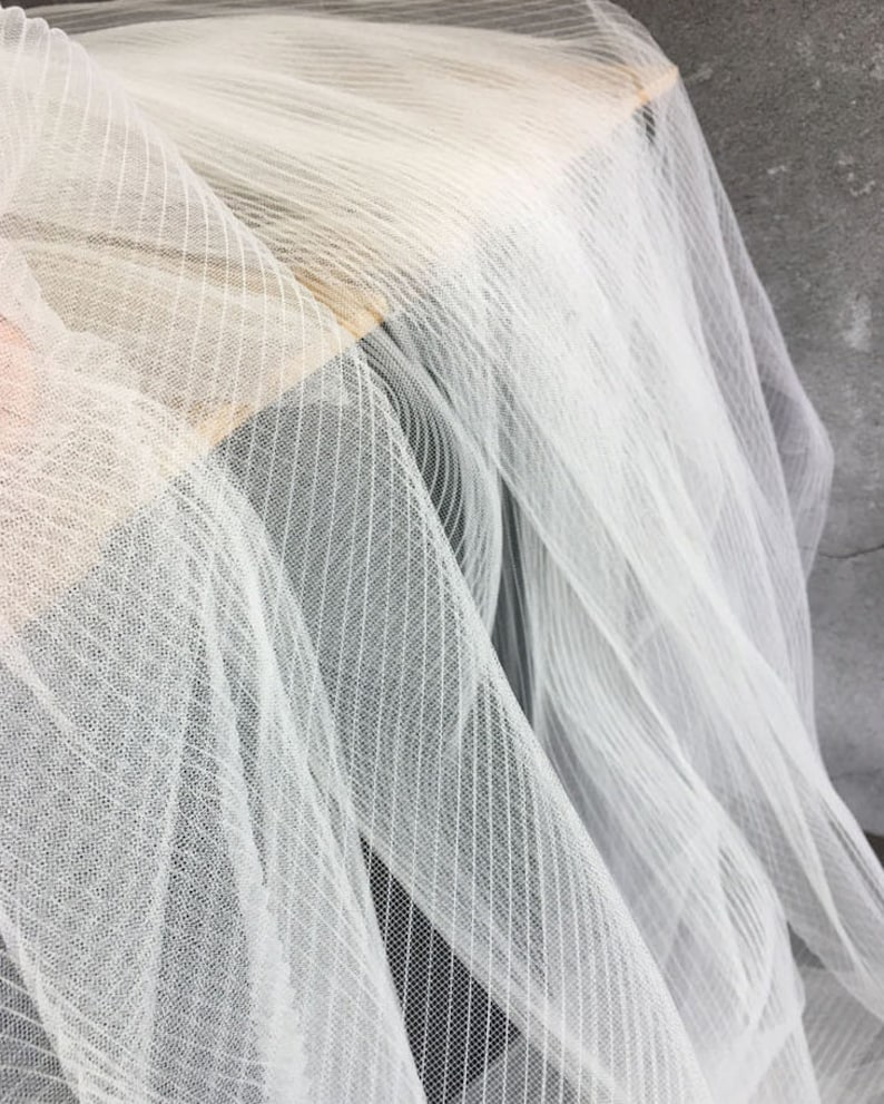 May include: White tulle fabric with a striped pattern. The fabric is soft and sheer, and it has a delicate texture.
