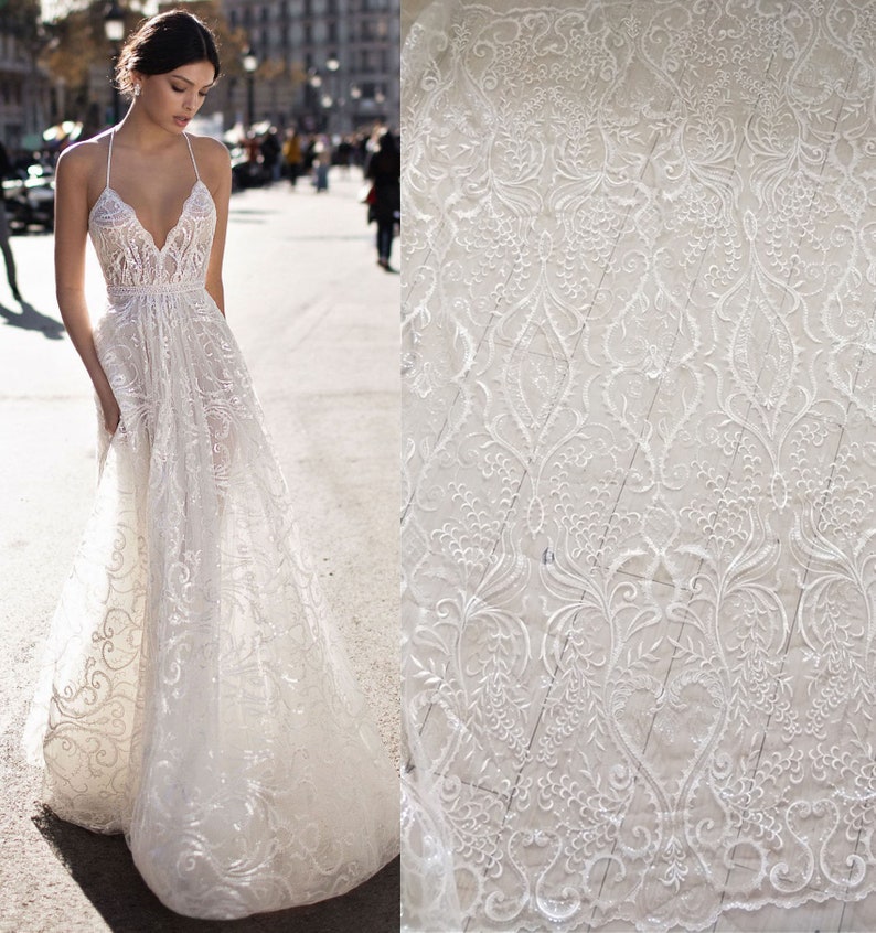 May include: White lace fabric with a delicate floral pattern. The lace is sheer and has a soft, flowing texture.