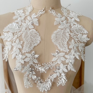 Op de afbeelding: Witte, met kralen en pailletten bezette kant-applicatie met een bloemenmotief. De applicatie is op een dunne tule en is perfect om een ​​toets van elegantie toe te voegen aan elk kledingstuk.