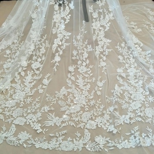 以下が含まれることがあります： 白い花柄のレース生地にスパンコールが施されています。レースは繊細な花柄で、全体に小さなスパンコールが散りばめられています。生地は透き通っていて軽量です。