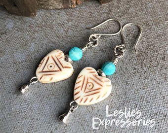 May include: A pair of silver heart-shaped earrings with turquoise beads and a carved design. The earrings are hanging from silver hooks.