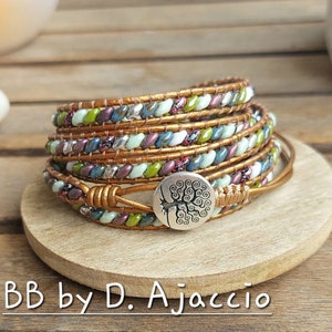Peut inclure: Un bracelet en cuir multi-rangs avec un charme en argent représentant un arbre. Le bracelet est composé de perles colorées, notamment vertes, bleues, violettes et blanches.