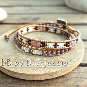 Peut inclure: Un bracelet enroulé avec un motif de perles crème, bordeaux et or. Le bracelet est enroulé autour d'une surface en bois. Le bracelet a un fermoir magnétique et est en cuir. Le texte "BB by D. Ajaccio" est visible sur la surface en bois.