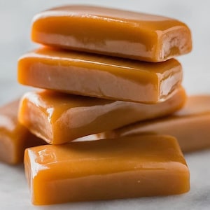 May include: A stack of four caramel candies, each with a smooth, glossy surface. The candies are a rich, golden brown color and have a slightly rectangular shape.