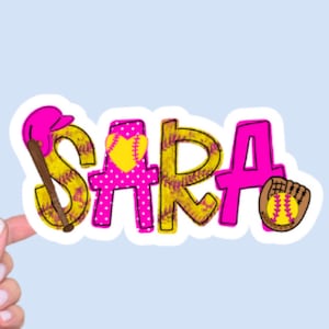 May include: A sticker with the name "SARA" in a playful softball theme. The letters are a mix of pink and yellow, with a baseball bat, a softball, and a glove incorporated into the design.