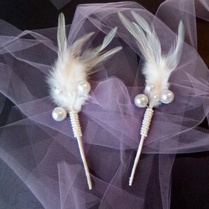 May include: Two white feather hair clips with pearl accents on a purple tulle background.