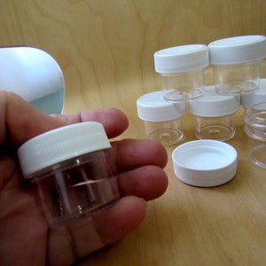 May include: A set of seven small, clear plastic jars with white lids. The jars are approximately 2 inches tall and 1.5 inches in diameter. The jars are perfect for storing small items, such as beads, buttons, or spices.