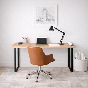 May include: A home office setup with a light wood desk, black metal legs, and a brown leather office chair. A black desk lamp, laptop, phone, and pencils are on the desk. A framed architectural drawing is on the wall.