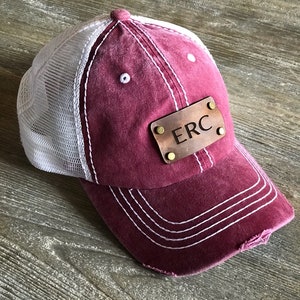 May include: Burgundy and white baseball cap with a mesh back and a brown leather patch with the initials "ERC" on it.