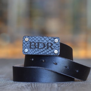 May include: A black leather belt with a silver buckle. The buckle is engraved with the initials "BDR".