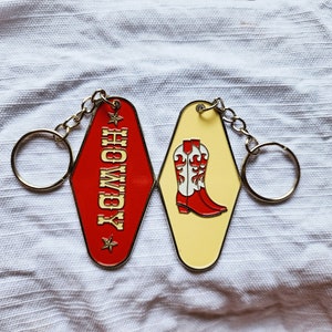 May include: A red and yellow metal keychain with a motel key tag that says "Howdy" and a second key tag with a pair of red cowboy boots with white accents.